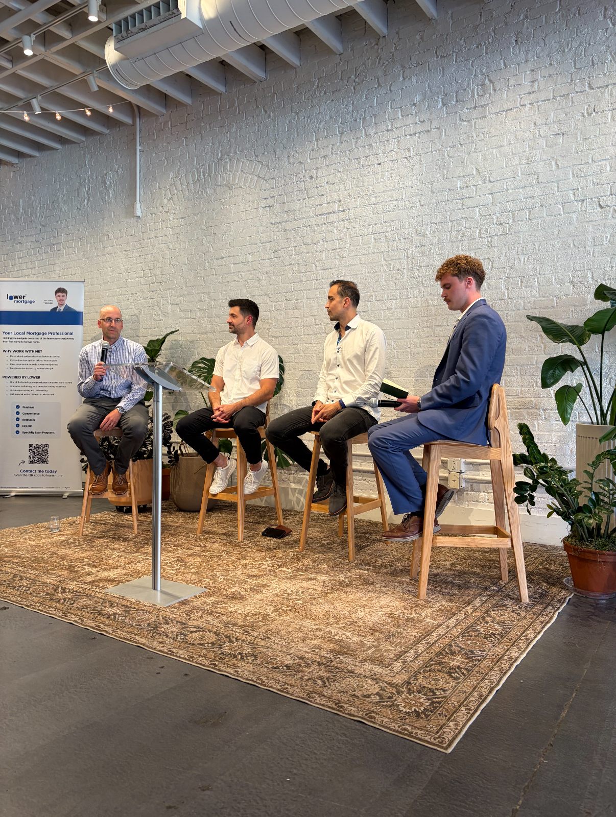 Four panelists on stage against a white brick wall